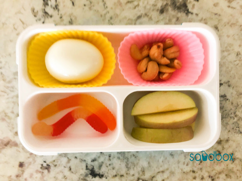 bento box with hard-boiled egg, gummy worm, apple slices, and cashews