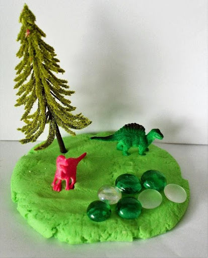 green play dough with dinosaurs, trees, and small glass beads used to benefit speech development